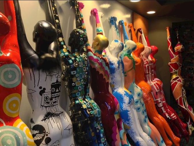 abstract painted mannequins in a row naked facing wall with hands overhead